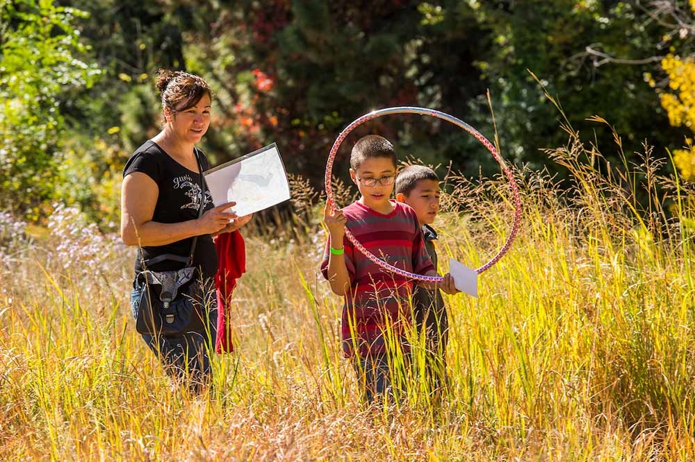 Adult and two children out in a high grass prairie field with a hula hoop