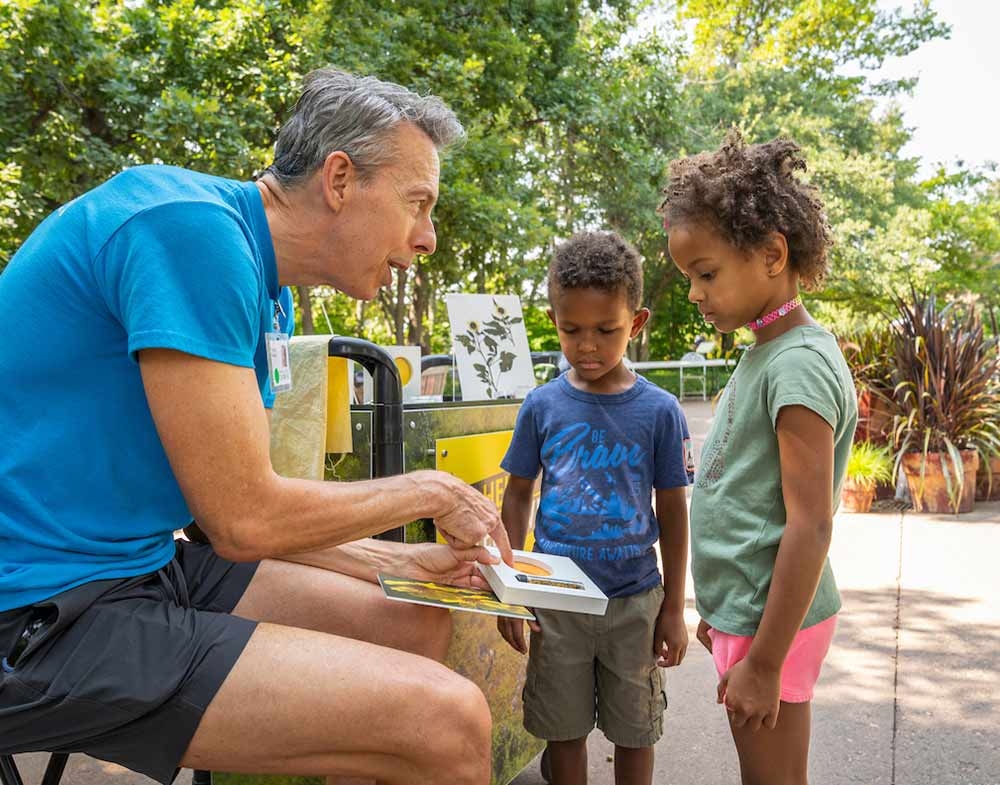 Adult in blue shirt showing two children a science project