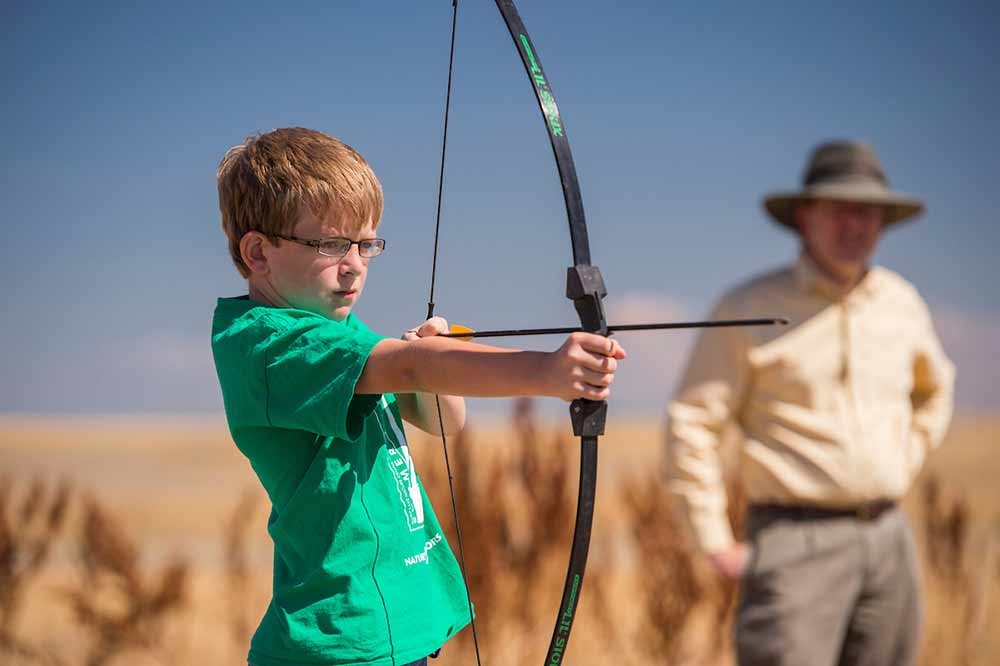 Culd with bow and arrow at Plains Conservation Center with adult in the background.