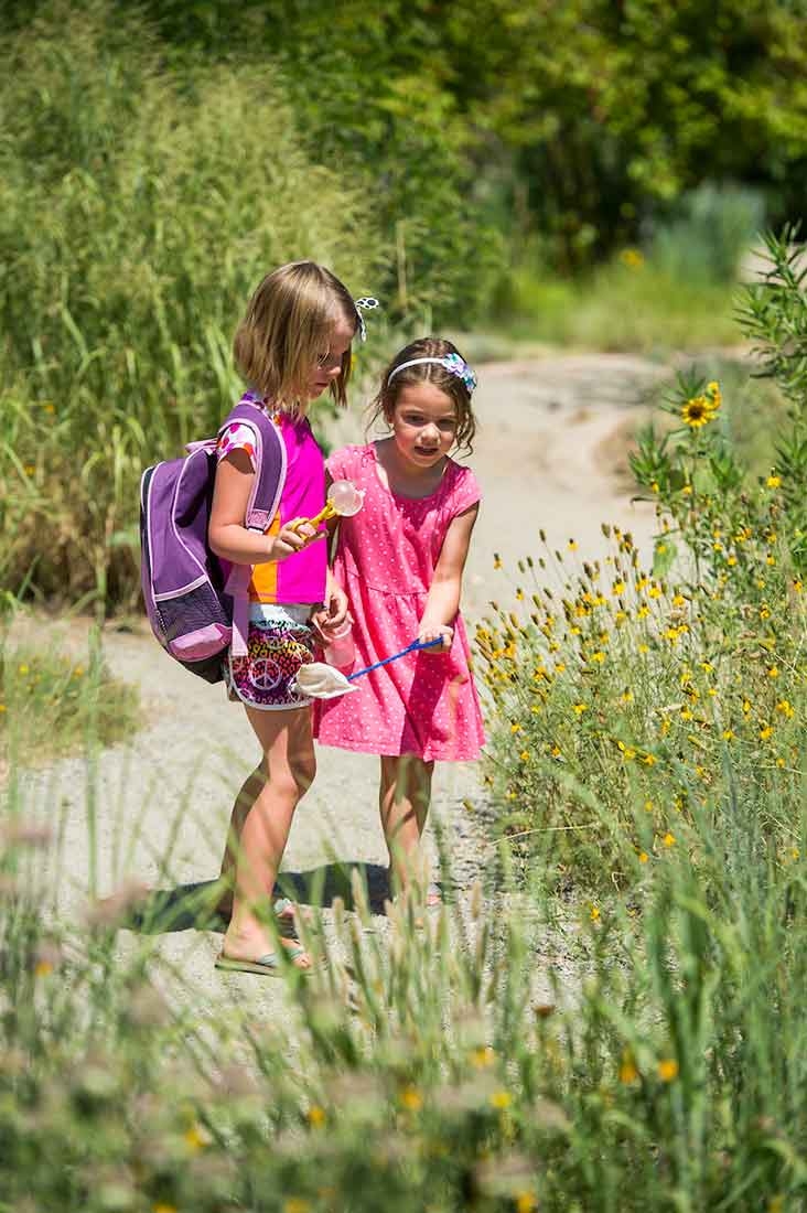 Two children wearing pink are pointing at plants.  