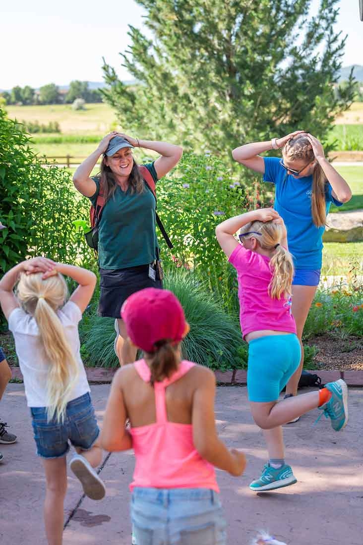 Two adults and three children playing a hopping game outside.