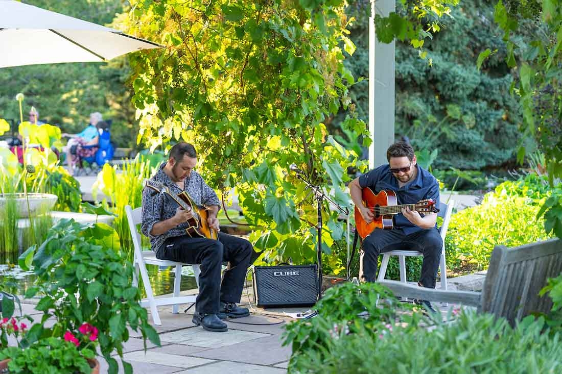 Two people playing guitars outside during Evenings al Fresco