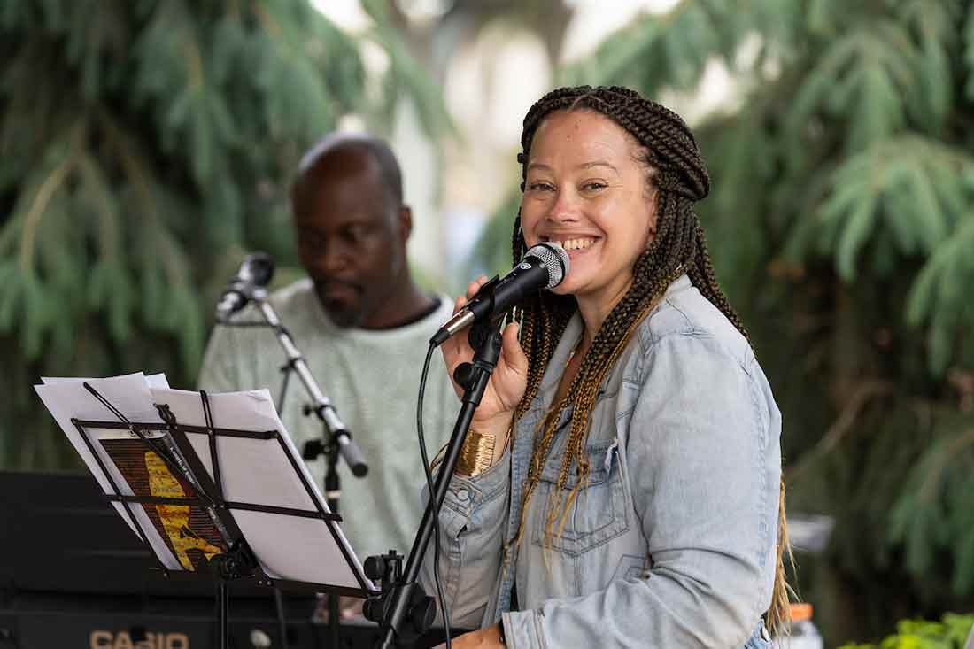 Woman smiling and holding a microphone with a man in the background with a microphone.