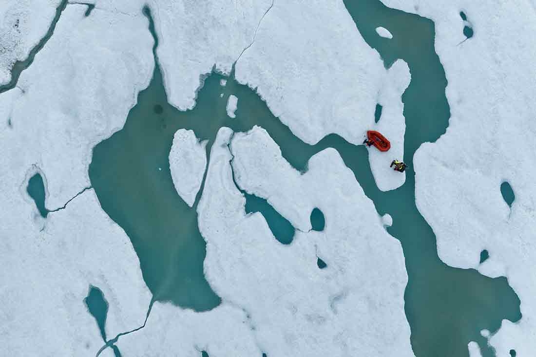 Two people cross pull their raft between the mainland and the northernmost land in the world, Inuit Qeqertaat (Kaffeklubben Island).