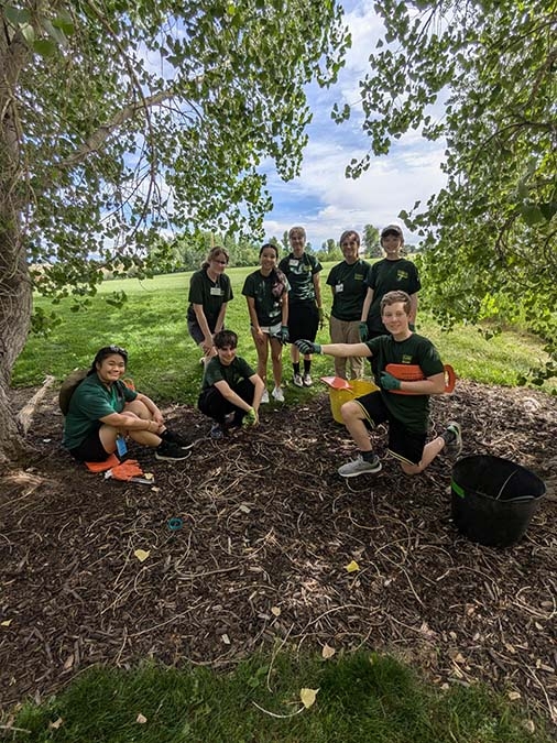 An intern with teen volunteers on a grassy area with mulch