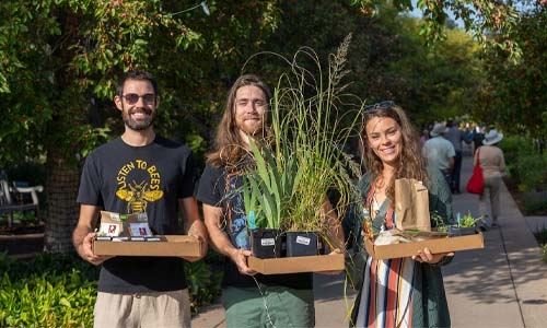 Three people holding plants purchased at sale